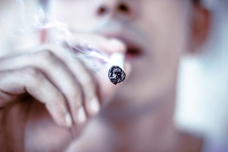 Gros plan sur visage et main, personne qui fume un joint