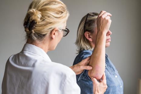 Médecin examinant le coude d'une patiente souffrant de psoriasis.