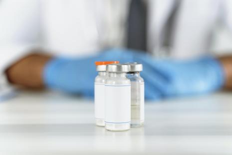 3 flacons de vaccin posés sur une table devant un soignant